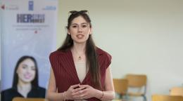 امرأة ترتدي قميصاً خمري اللون تتحدث أمام مجموعة من الأشخاص.