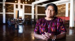 A woman is seated indoors and looking at the camera 