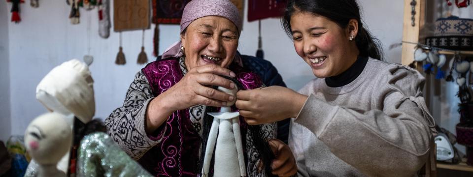 Two women smile while they put together a doll. 