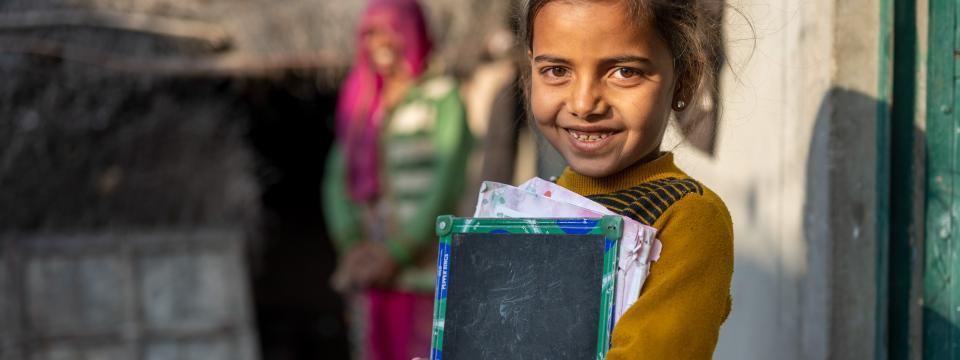 A young girl holds her school-work in her hands, in front of a house, at dusk.