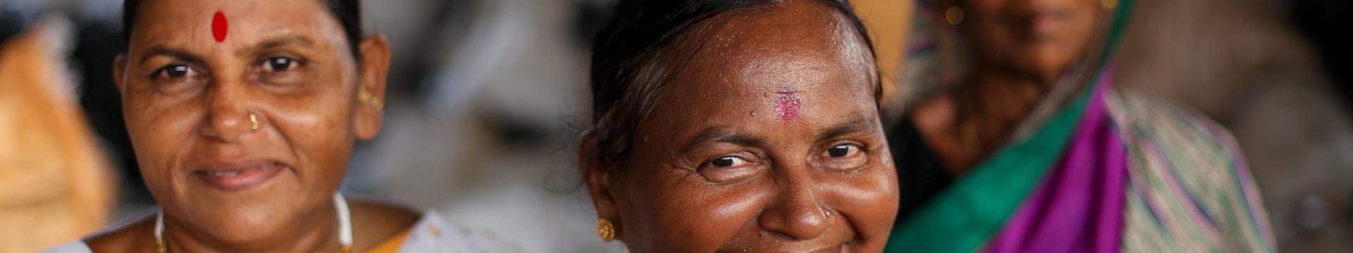 Three women in colorful saris stand in a triangle formation. 