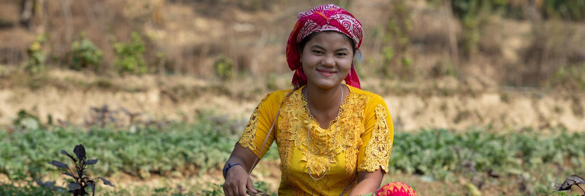 A woman sits with a basket in a green farm field. 