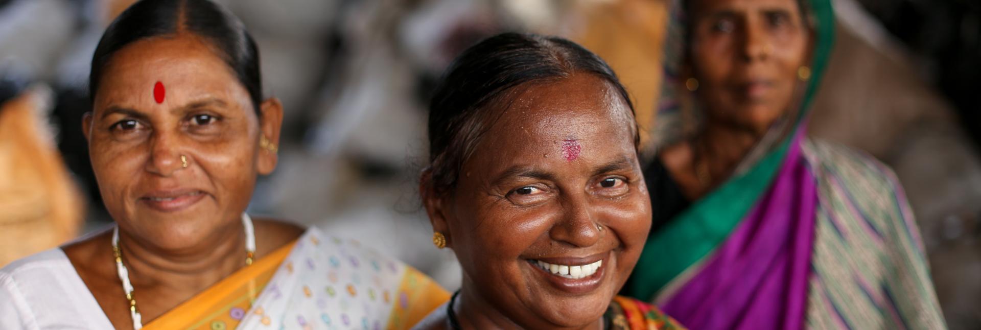 Three women in colorful saris stand in a triangle formation. 