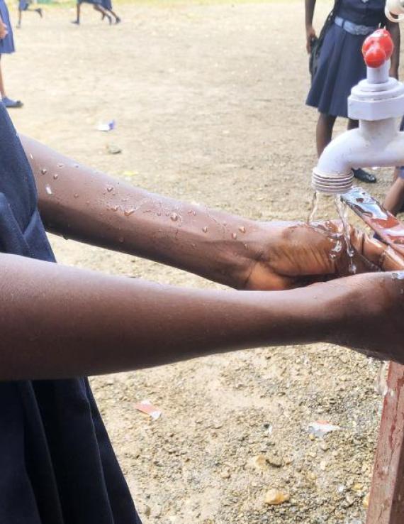 A girl in what seems to be a dark-blue school uniform washes her hands with soap outside.