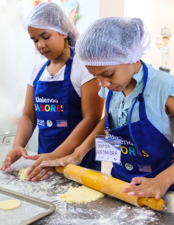 Two children roll a rolling pin on a baking sheet as they participate in a new UN programme