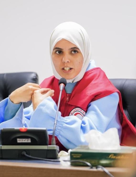 حياة، متطوّعة ترتدي سترة حمراء، تتحدث خلال اجتماع على طاولة للمؤتمرات.