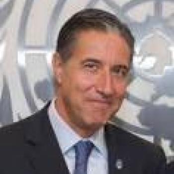 Оскар Фернандес-Таранко улыбается в камеру на фоне большого логотипа ООН.