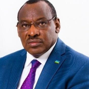 A man in a dark blue suit and purple tie with thin glasses.