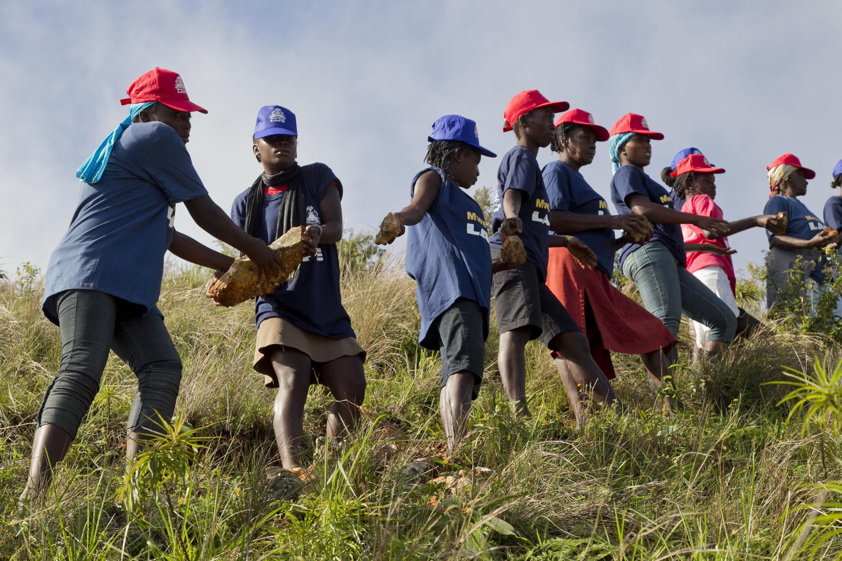 يصطف الرجال والنساء في خط تجميع ويمررون الصخور من شخص إلى آخر.