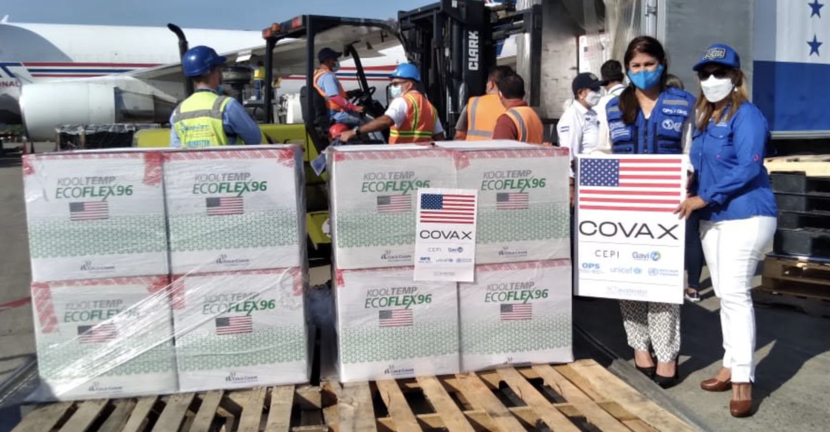 Varias personas descargan las vacunas contra la Covid-19 de los aviones, mientras dos mujeres sostienen un cartel del mecanismo COVAX.