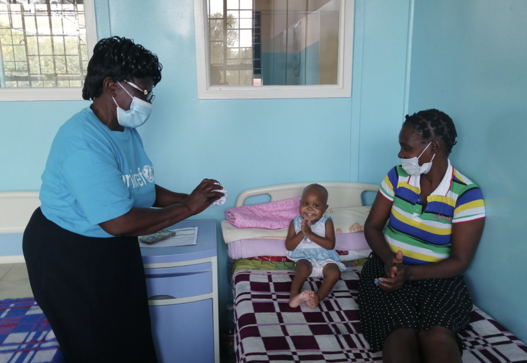 Una madre y su hijo sentados en una cama mientras hablan con una representante de UNICEF.