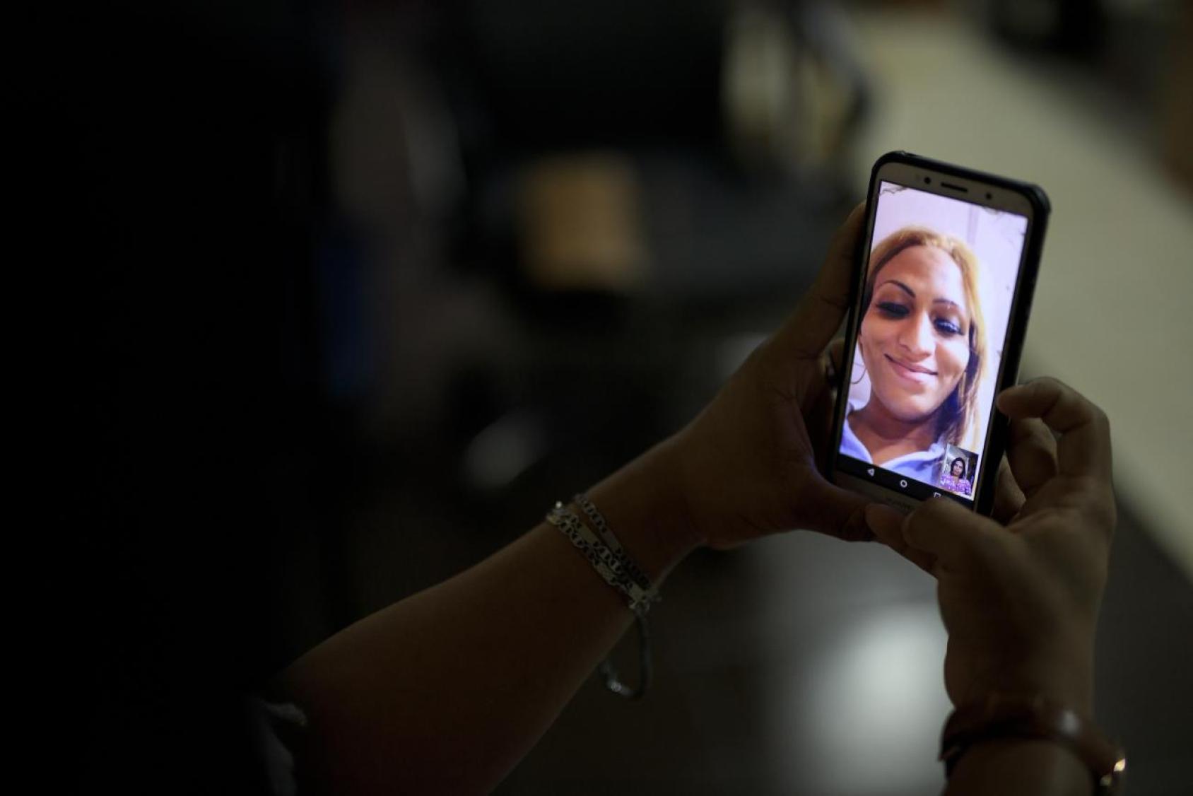 Una imagen de la mano de una persona sosteniendo un teléfono móvil, en el cual aparece la imagen de otra persona, en vio y directo.