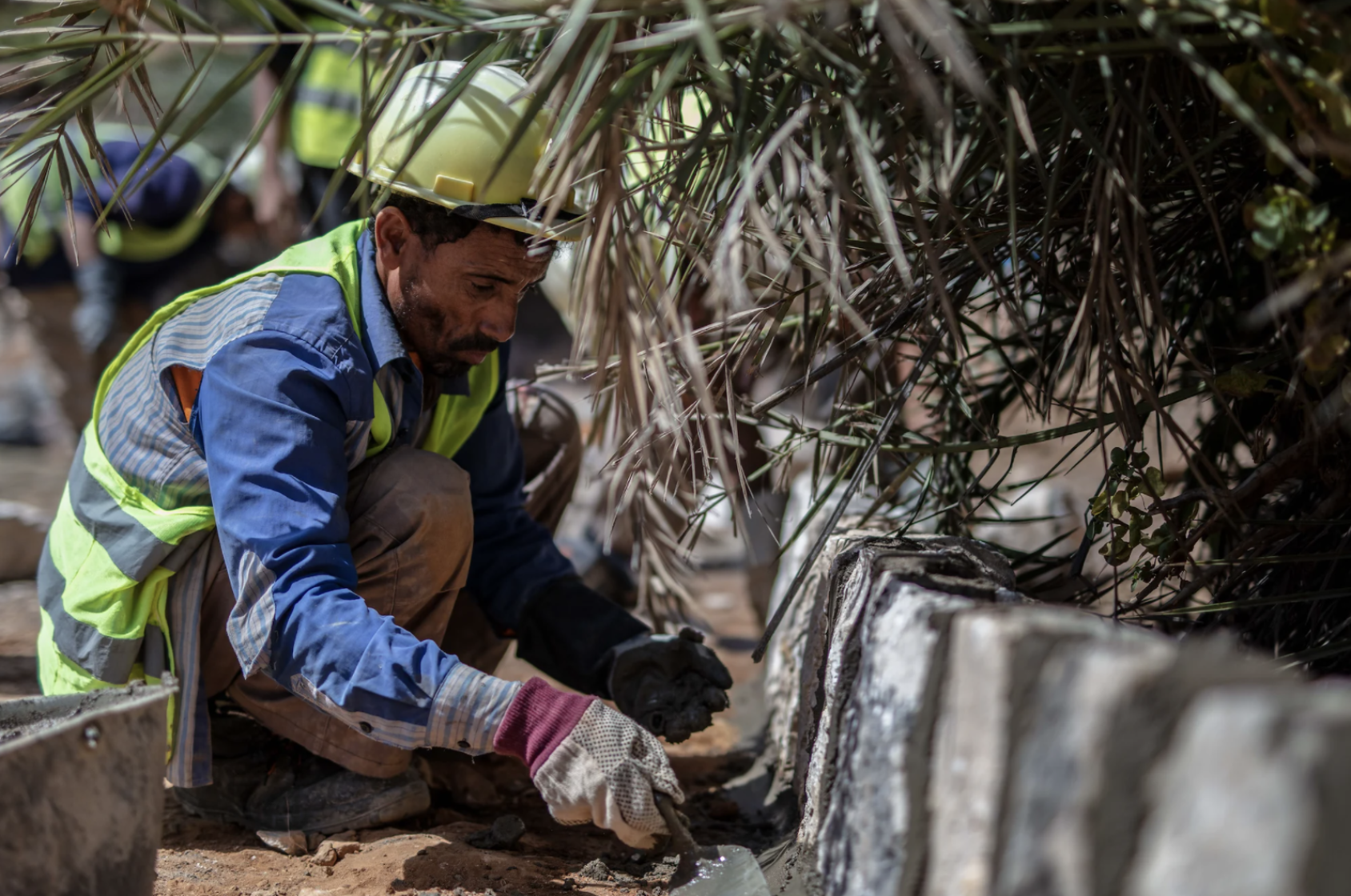 Gros plan sur un ouvrier, accroupi, travaillant à la réparation d'une route.