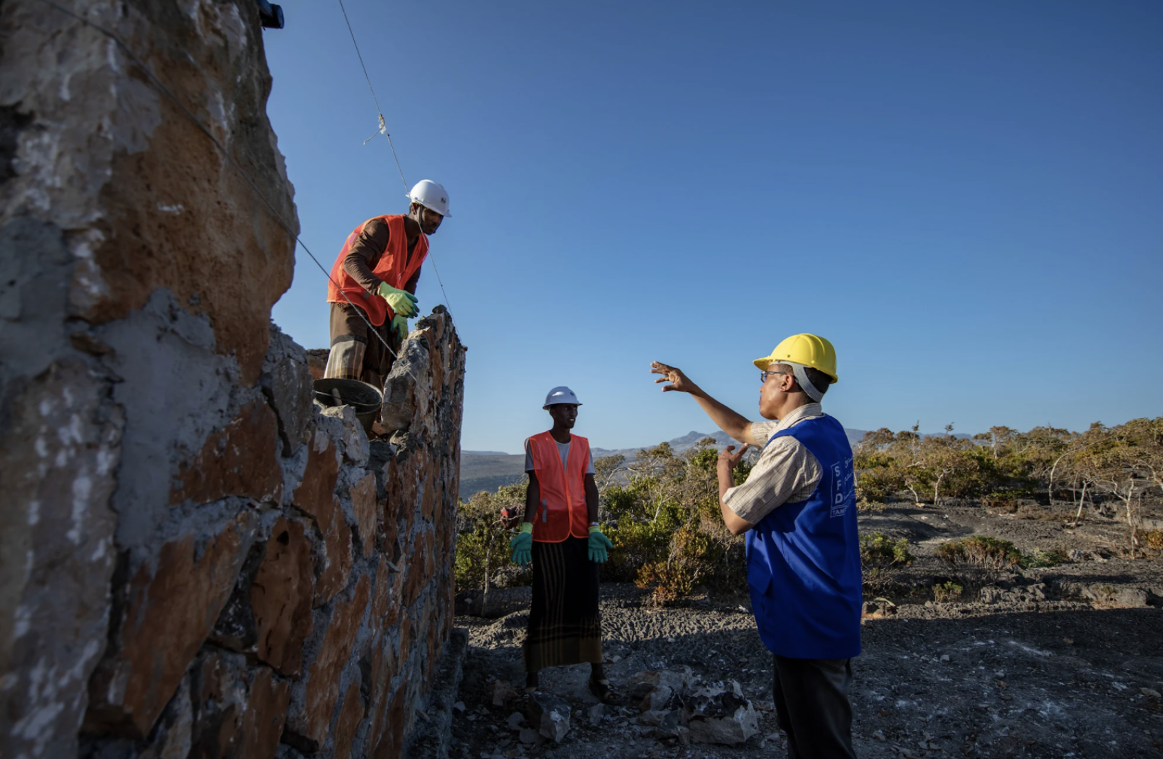Un ingénieur du bâtiment donne des consignes à deux ouvriers travaillant à la construction d'un réservoir d'eau.