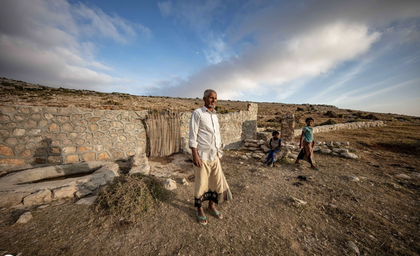 Un homme se tient debout près d'un réservoir d'eau de pluie en souriant. Deux enfants se tiennent près de lui.
