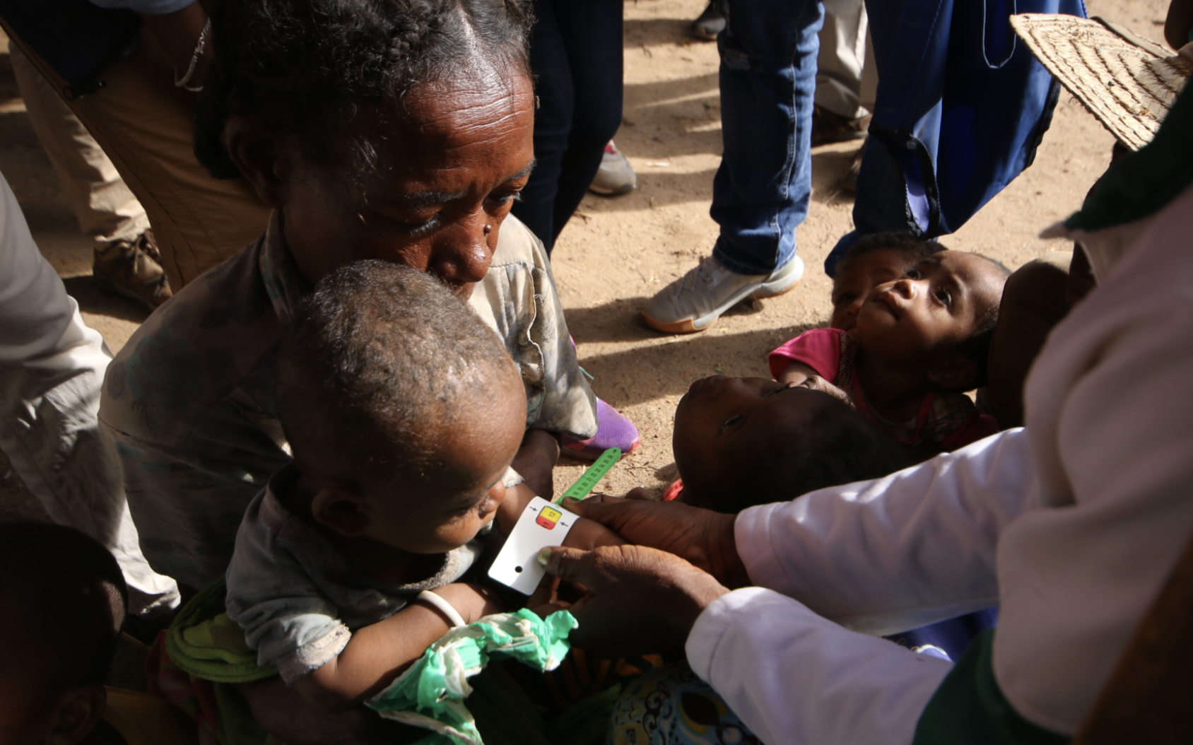 A woman holds a baby in her arms while they measure their wrist size to determine the level of malnutrition. 