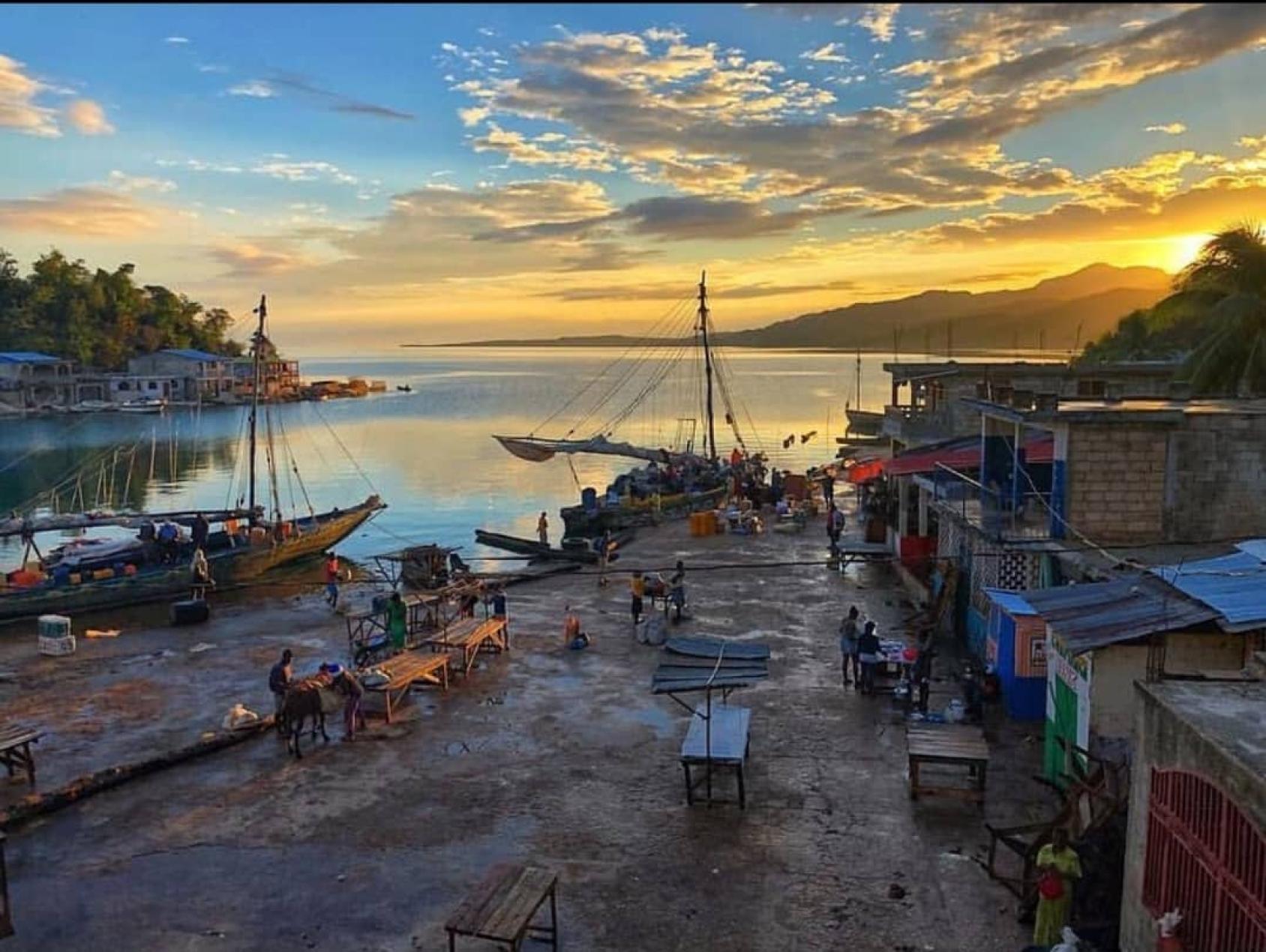 Au coucher du soleil, des personnes s'affairent autour de commerces alignés les uns à côté des autres sur une berge, dans la localité de Pestel, en Haïti.