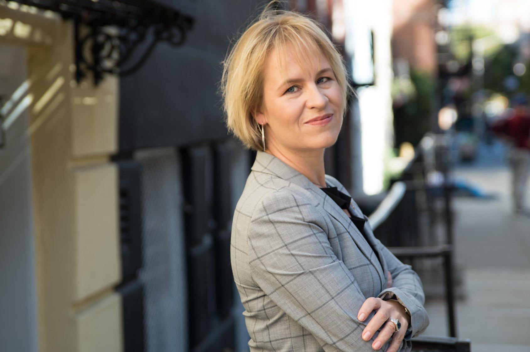 Une femme aux cheveux blonds coupés au carré, photographiée de profil, a la tête tournée vers l'objectif et sourit.