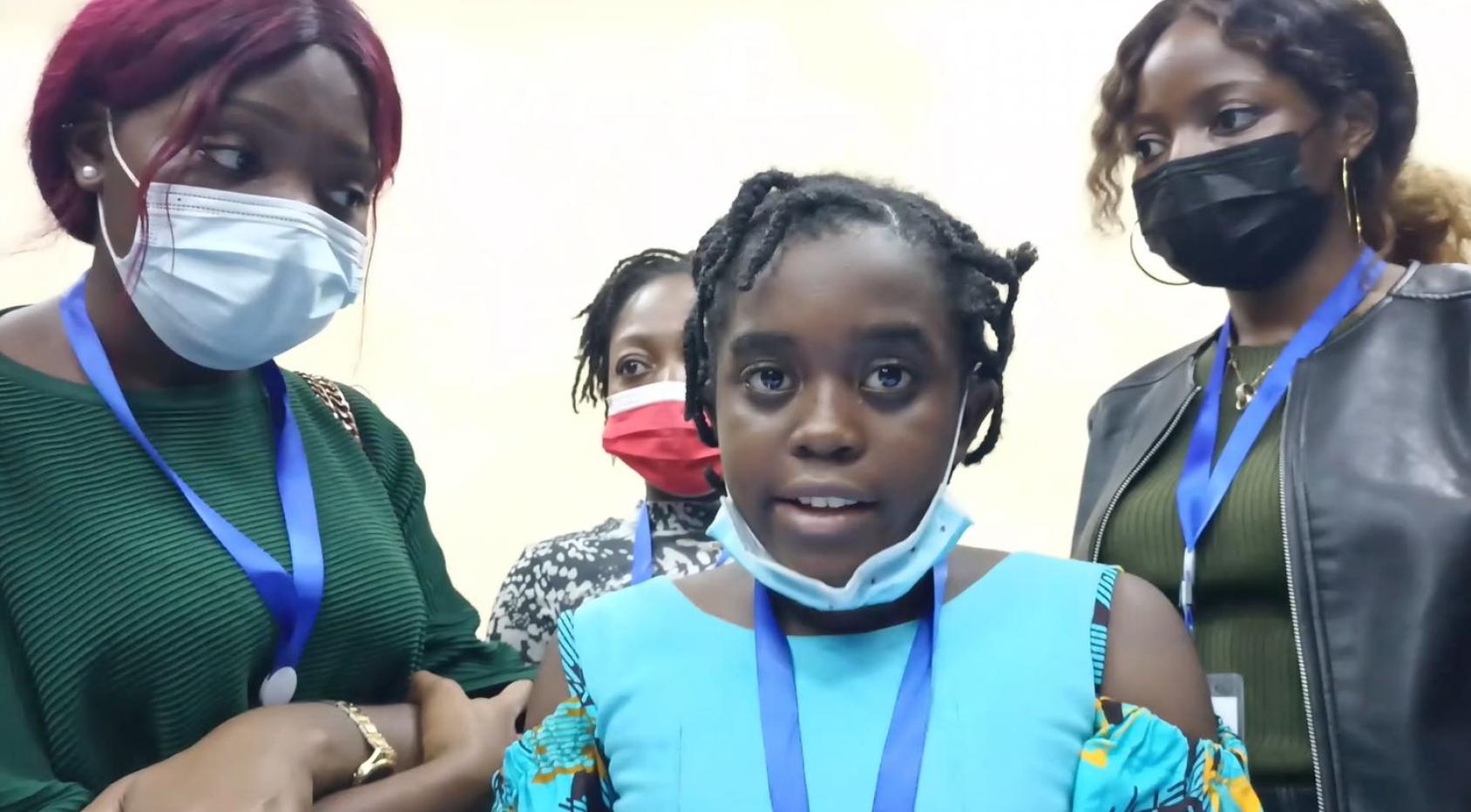 一个身穿浅蓝色衬衫的年轻女孩直视镜头，她旁边有另外三个女人。