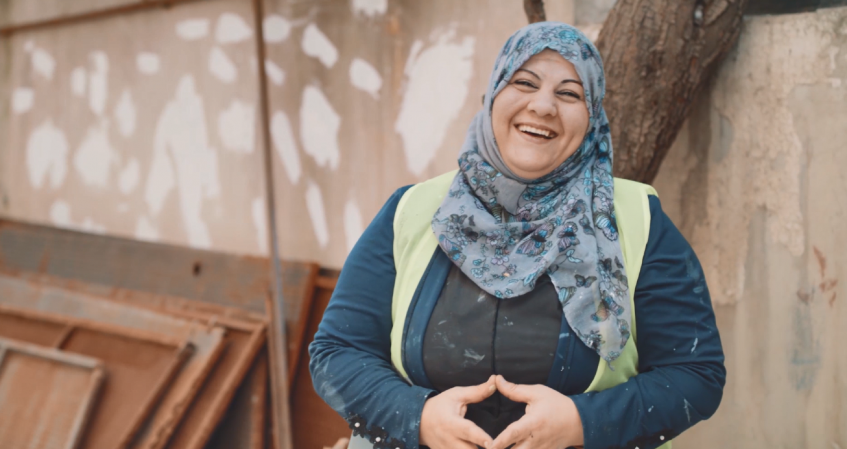 Une femme portant un foulard bleu autour de la tête et des épaules regarde l'objectif en riant.