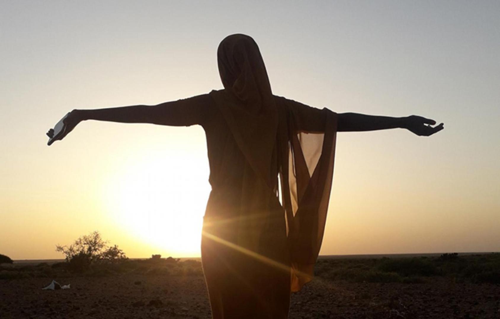 Une silhouette de femme, dos à la caméra, regarde un coucher de soleil en levant les bras.