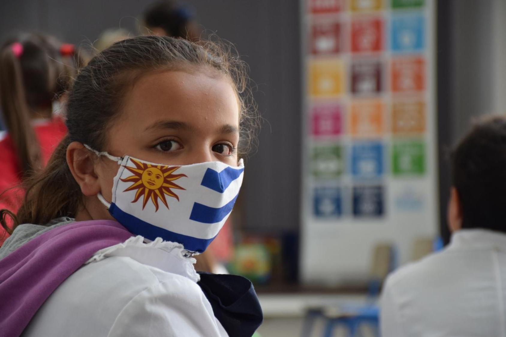 Una niña mira a la cámara con una mascarilla con la bandera de Uruguay.
