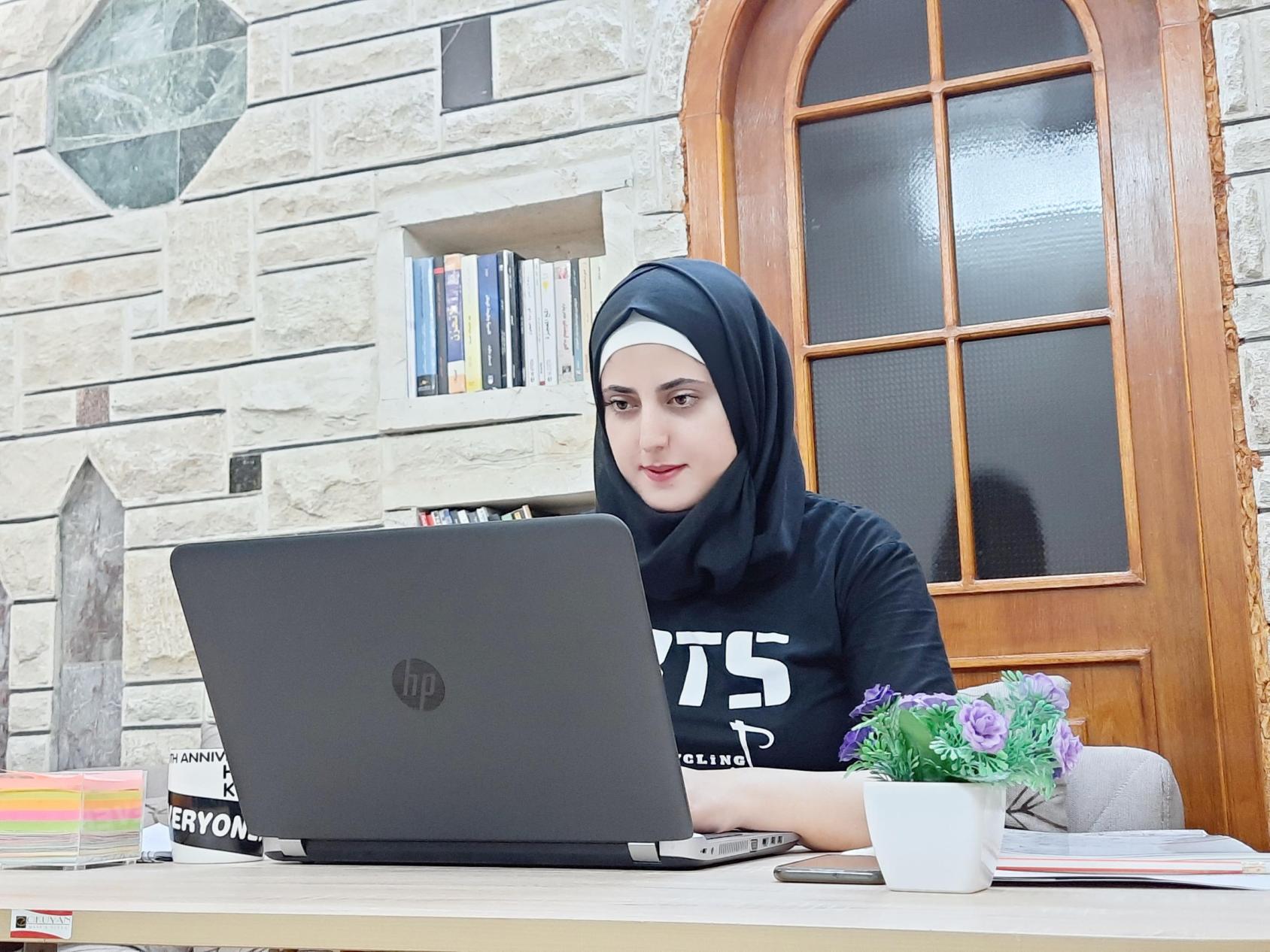 一名年轻女子坐在窗前的电脑前。