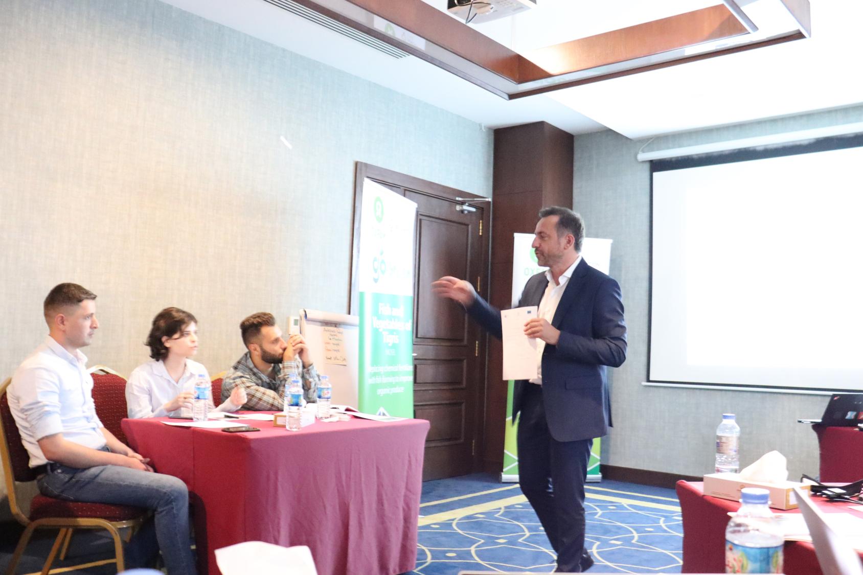 一个人对坐在一张有红色桌布的桌子旁的三个年轻人说话。