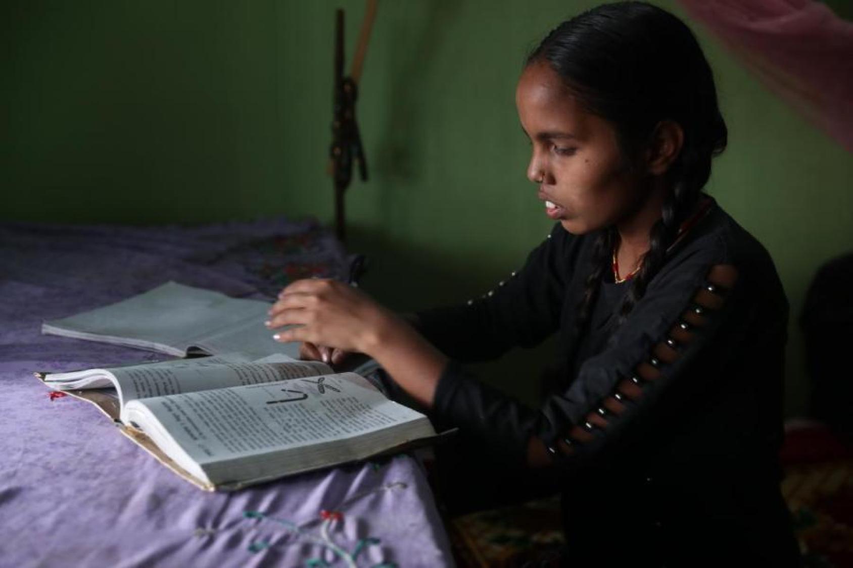 A young girl looks down at her books at a table with a purple tablecloth. 