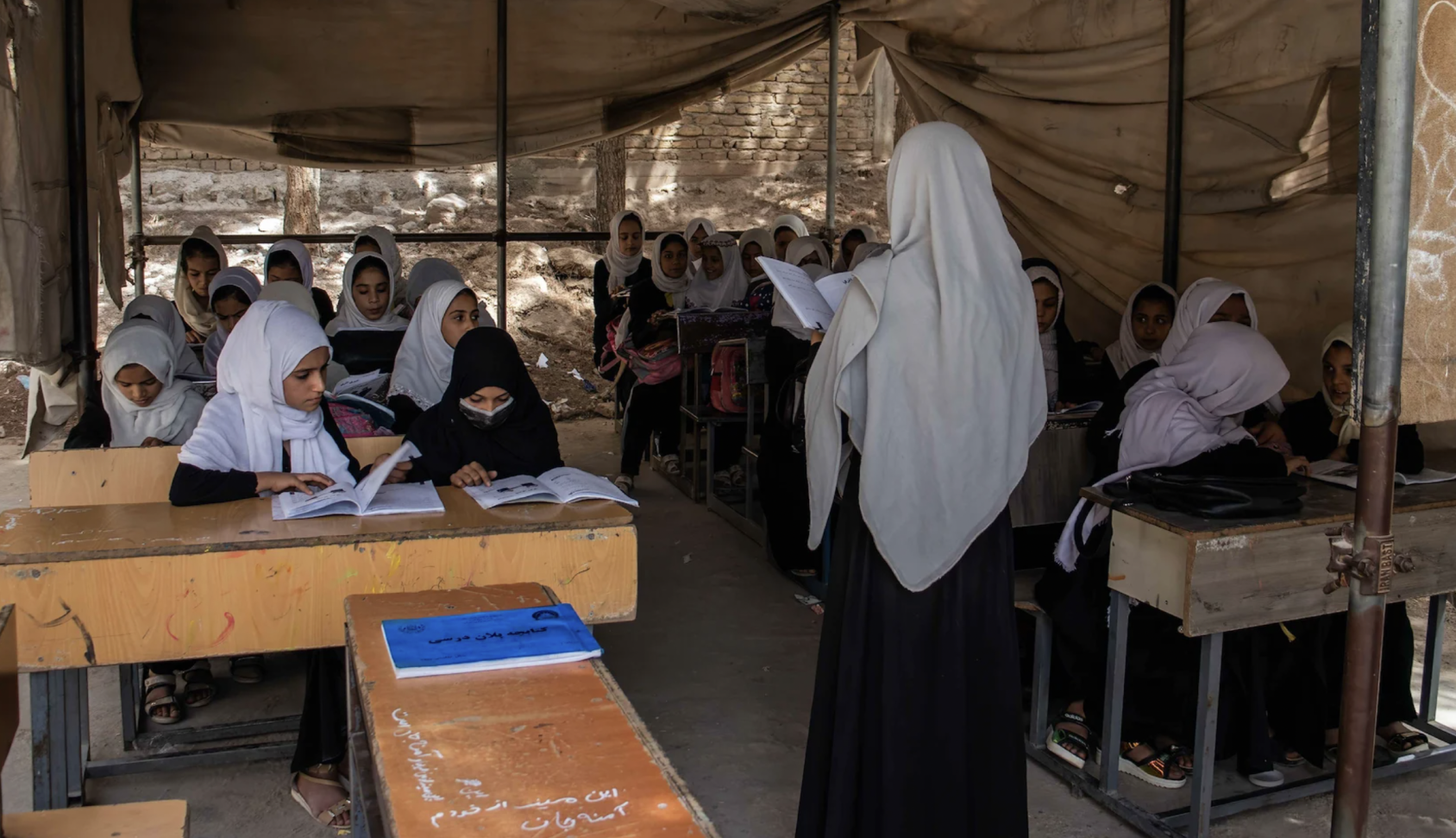 A group of children sitting at desks with a teacher at the front of the class. 