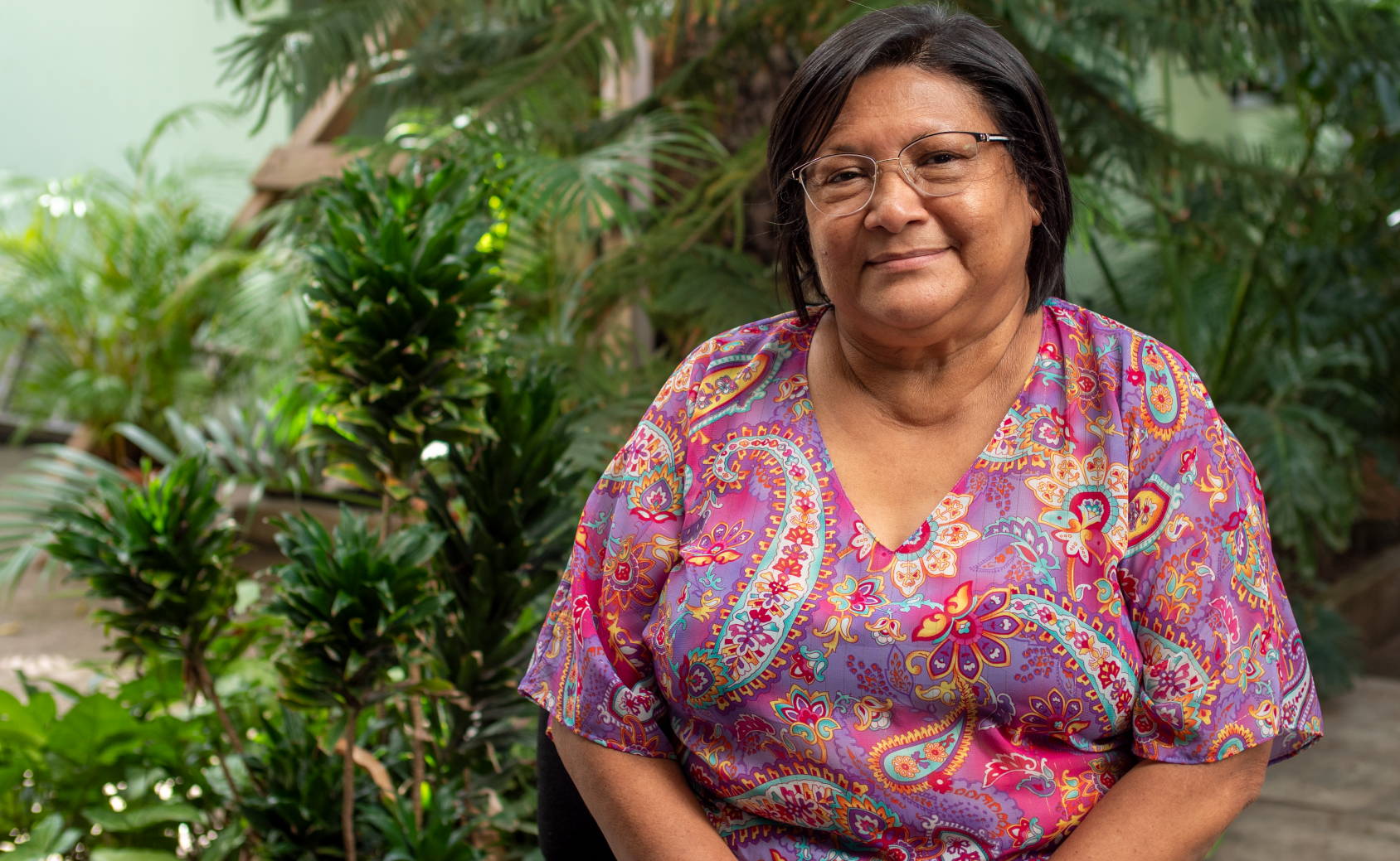Ana, smiles warmly as she poses sitting in front of small trees. 