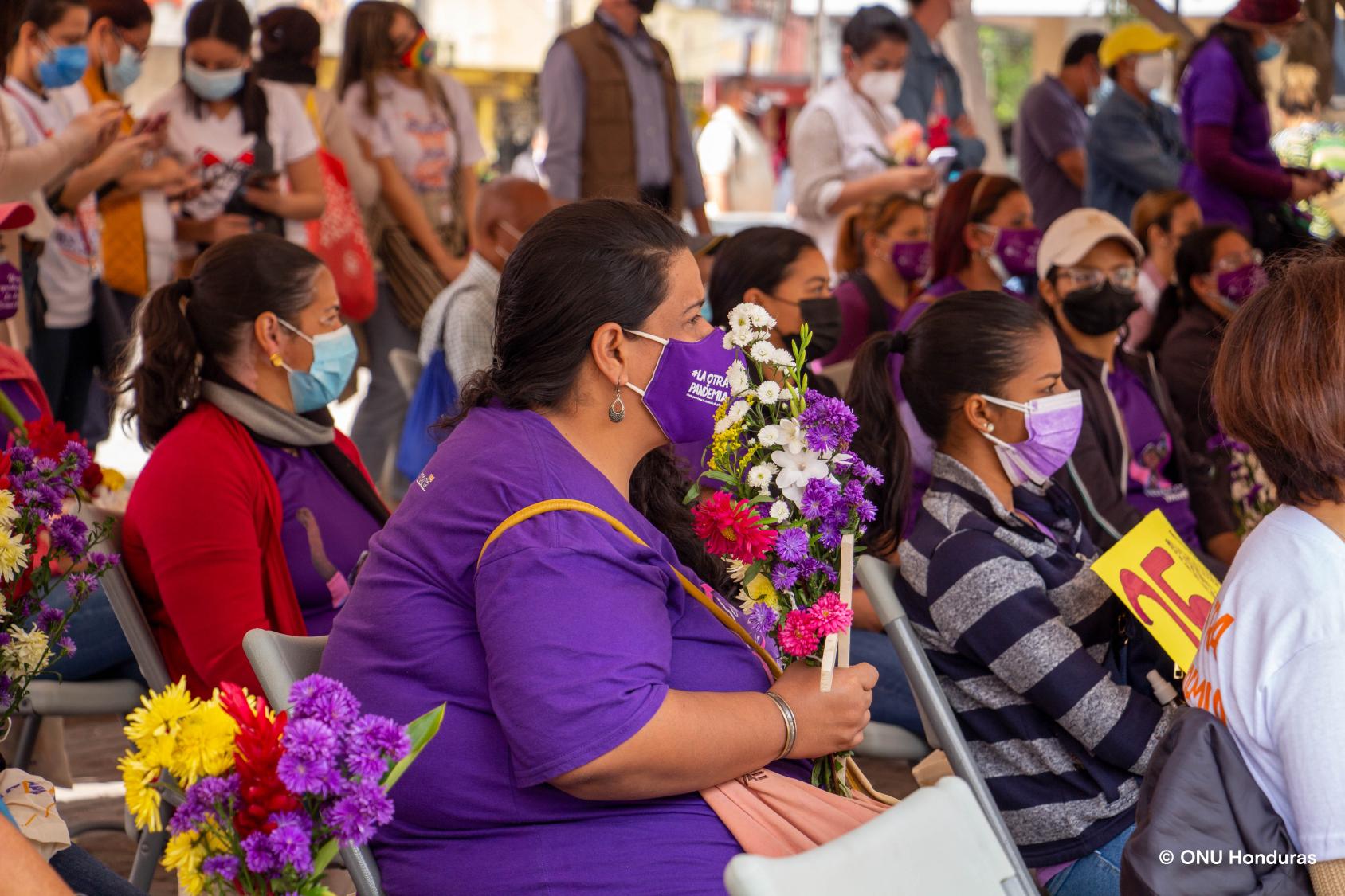 Women wearing masks sit carrying signs, flowers and crosses representing those victims of abuse. 