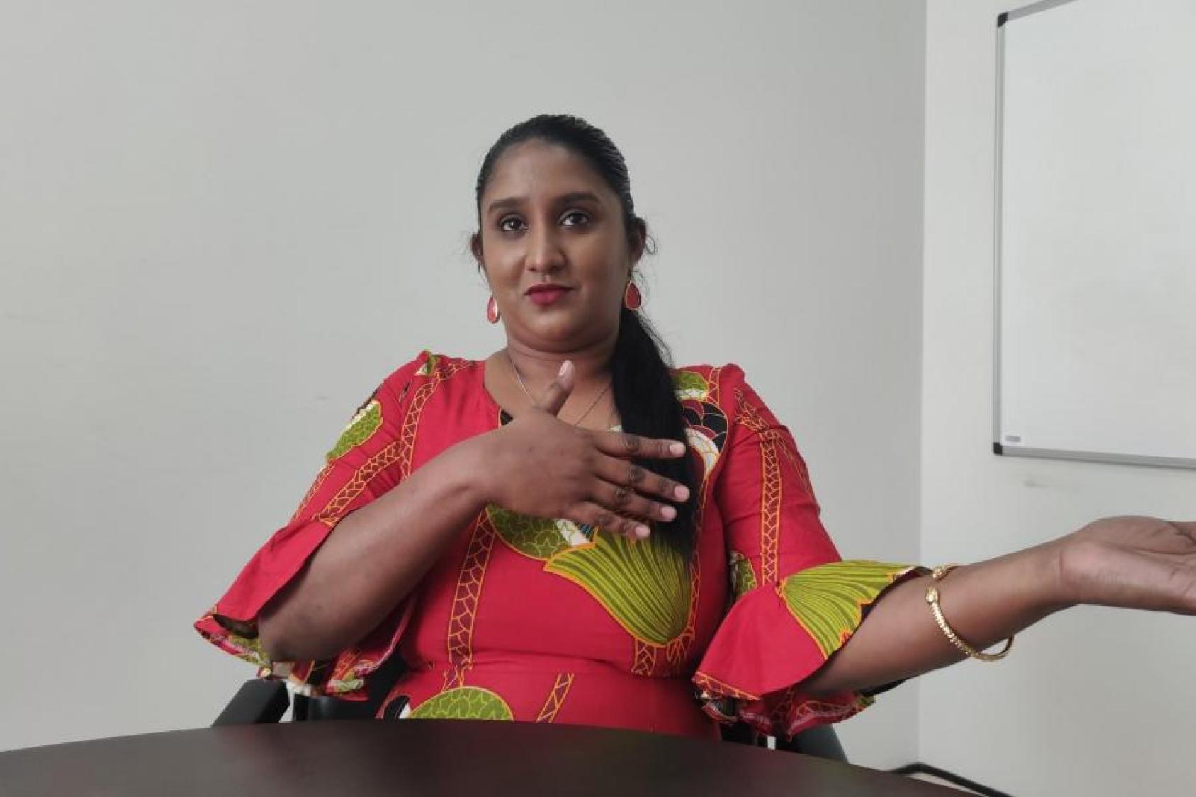 一位身着彩色礼服的妇女坐在桌前，同时直视着镜头。