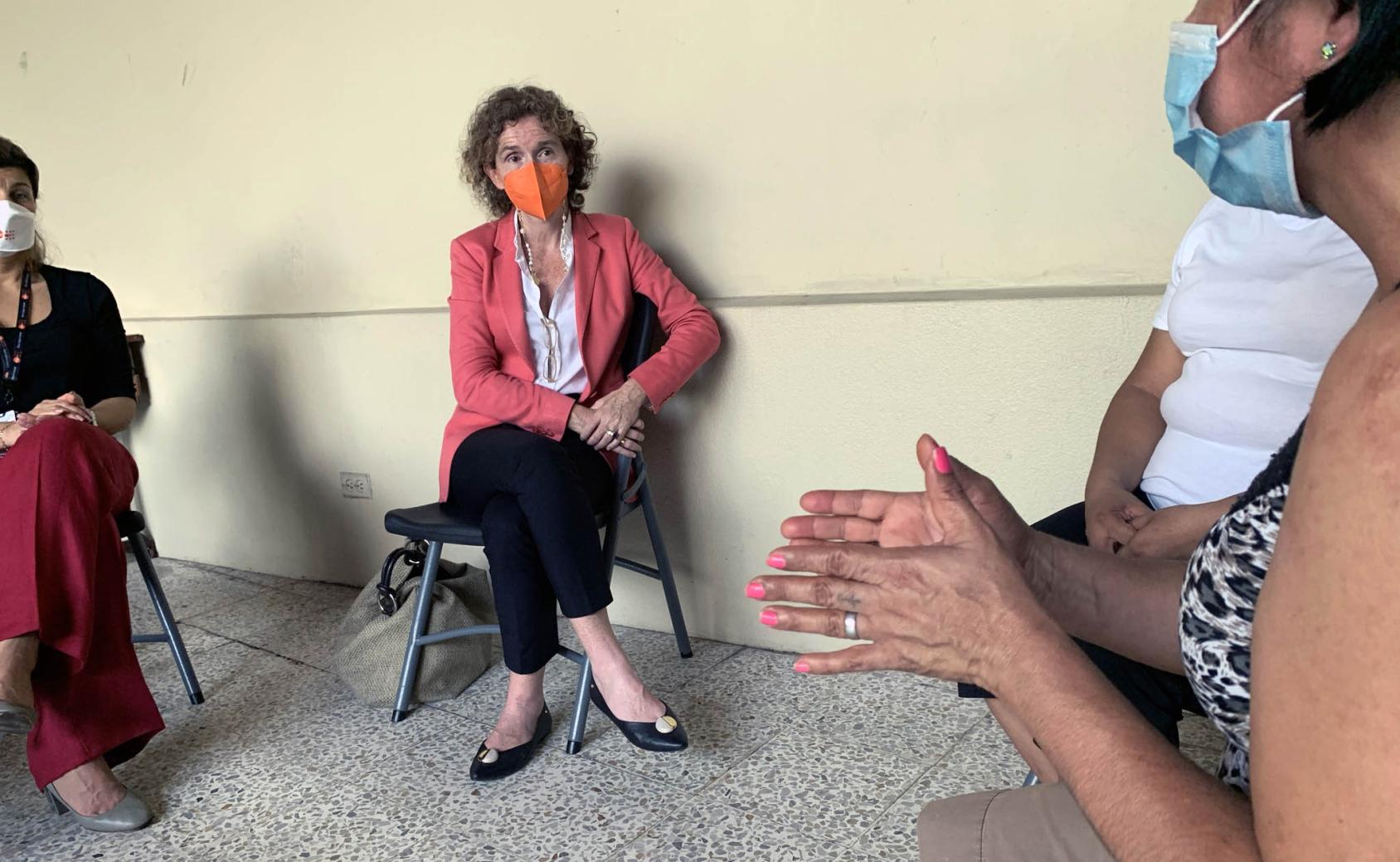 RC sits in the centre, wearing a mask, as she listens to women share their stories. 