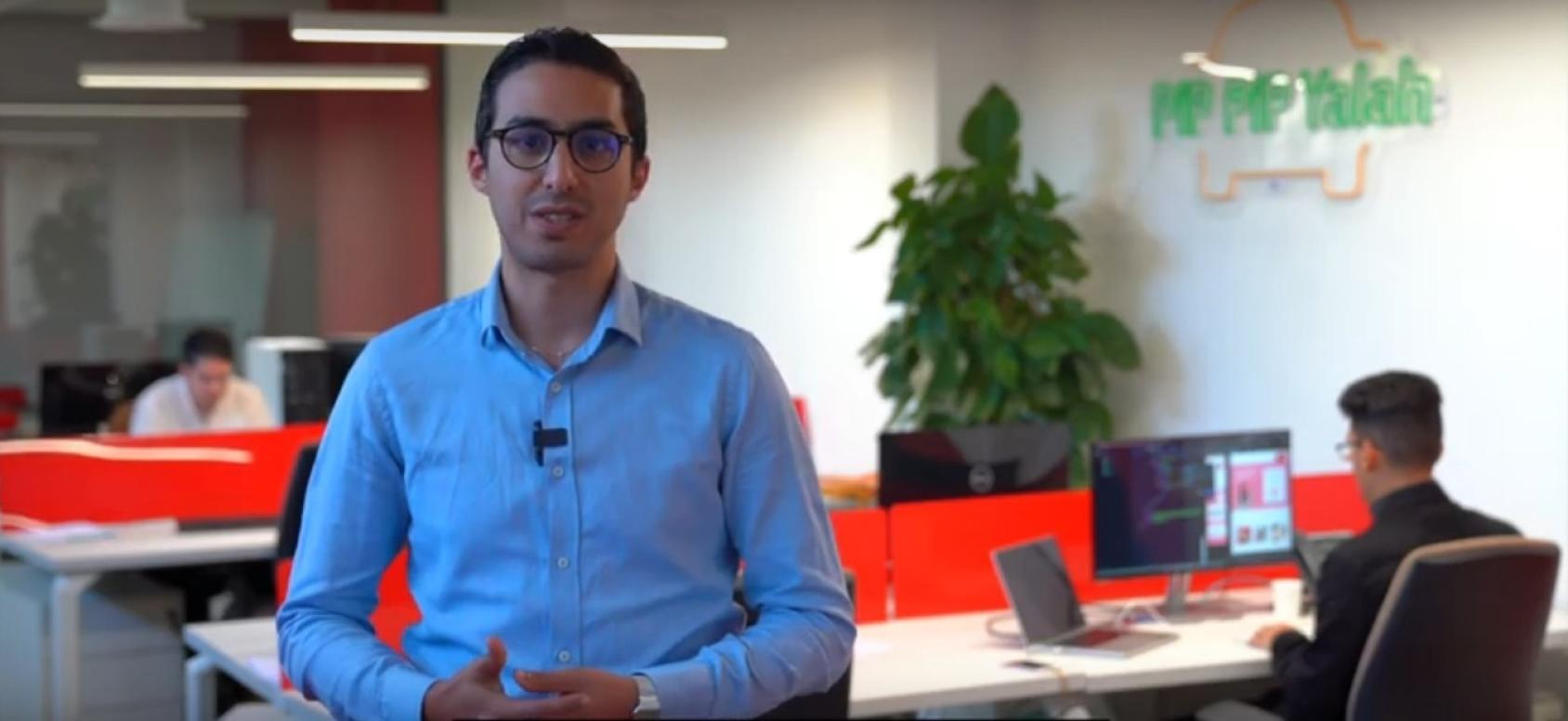 一个穿着蓝色纽扣衬衫、戴着黑色眼镜的男人直视着镜头。