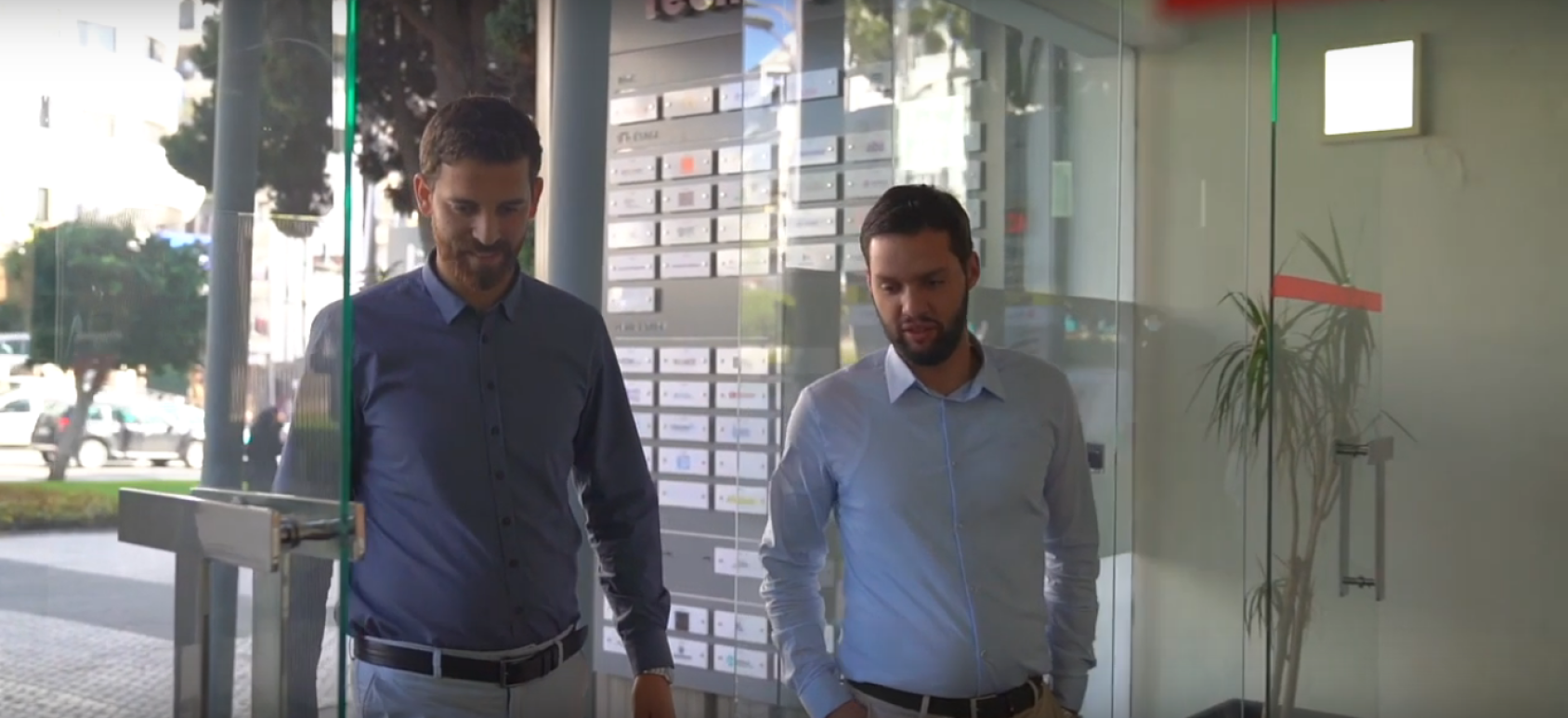 两个穿着扣子衬衫的男人穿过一扇玻璃门。