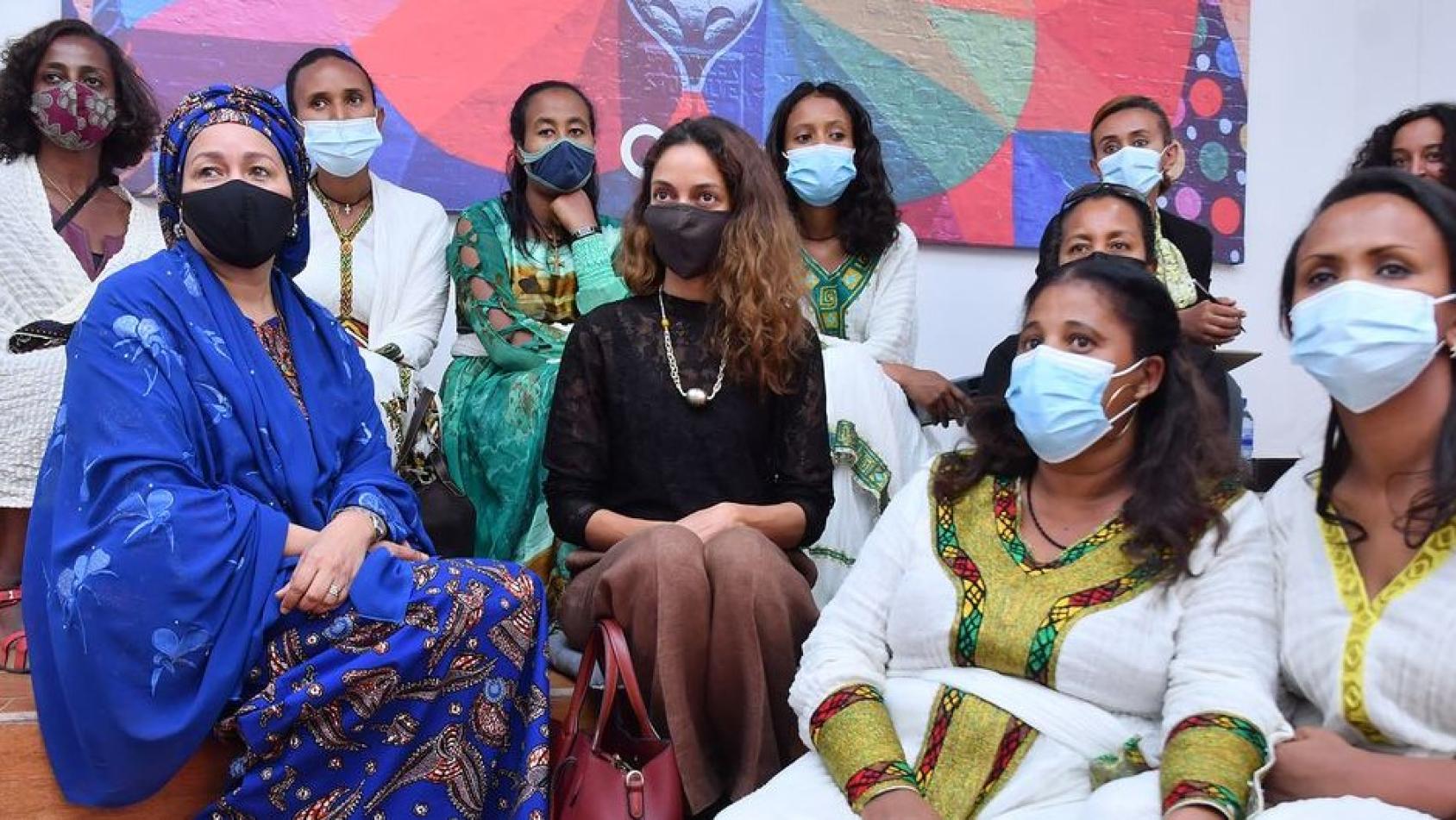 Deputy Secretary-General Amina Mohammed with protective facemask surrounded by a group of sitting young women wearing facemasks.