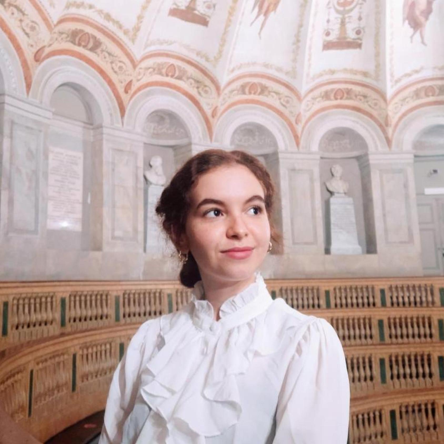 Portrait d'une jeune fille marocaine en chemisier blanc se debout dans une grand salle majestueuse et regardant fièrement vers la gauche.
