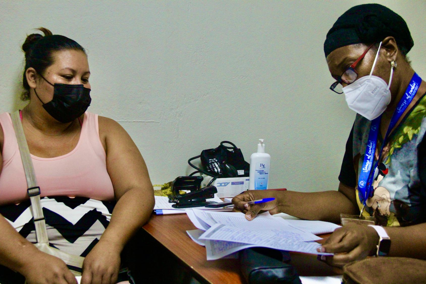 Une infirmière est assise à son bureau et discute avec une patiente.