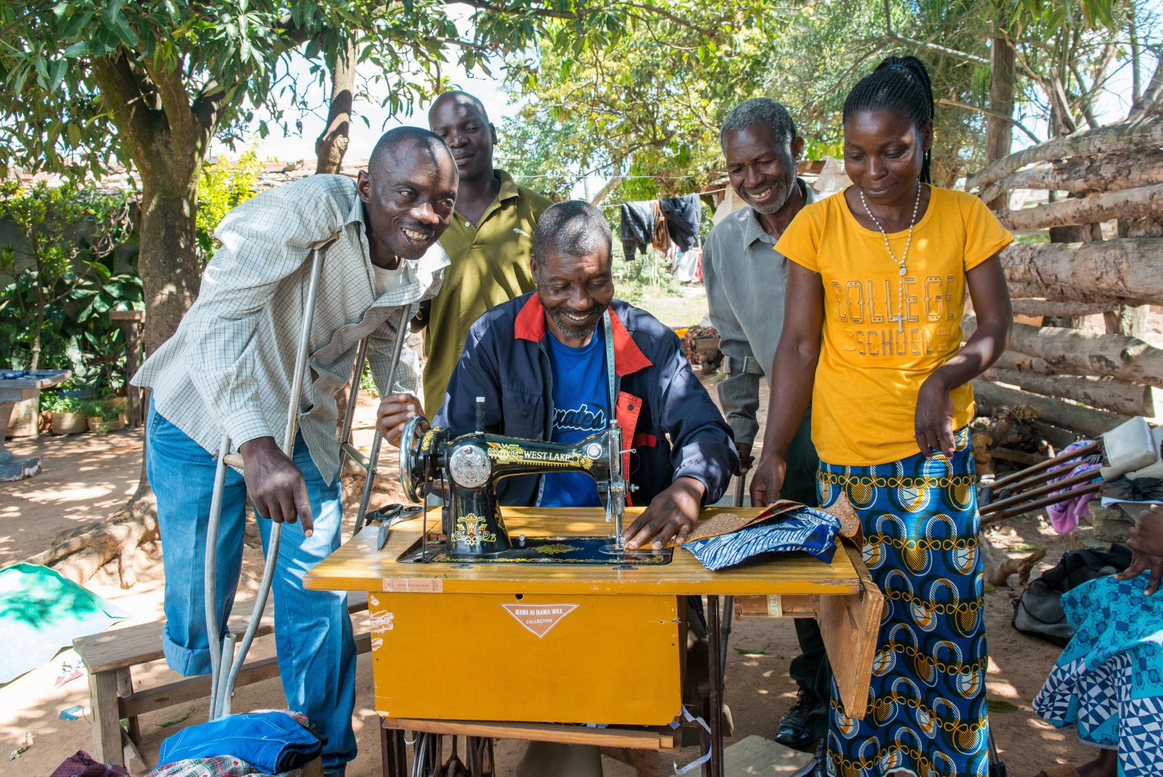 Grupo de personas rodeando a un hombre que trabaja en una máquina de coser.