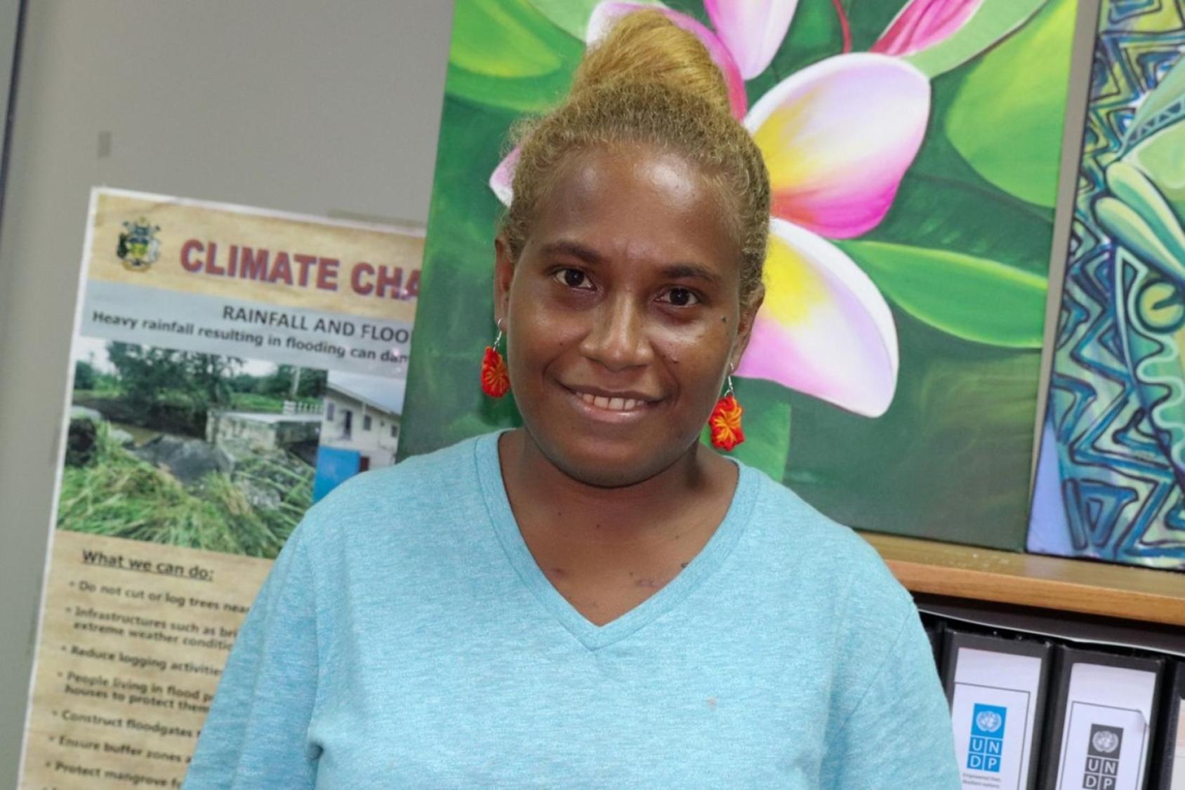 Aux Îles Salomon, une jeune femme militante portant un haut bleu ciel et des boucles d'oreilles rouges sourit à la caméra.