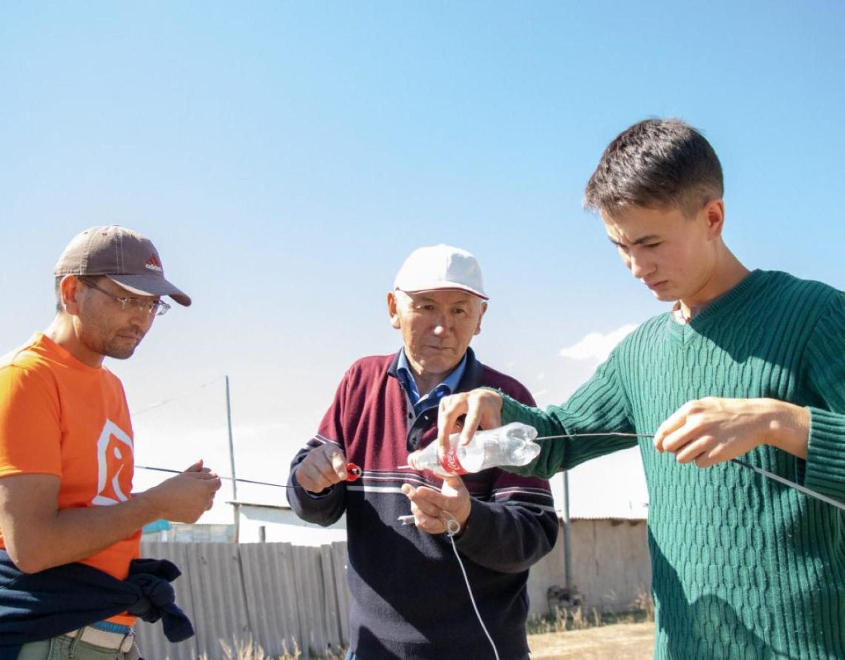 Three men covering connection wires to protect those from the harsh weather conditions.