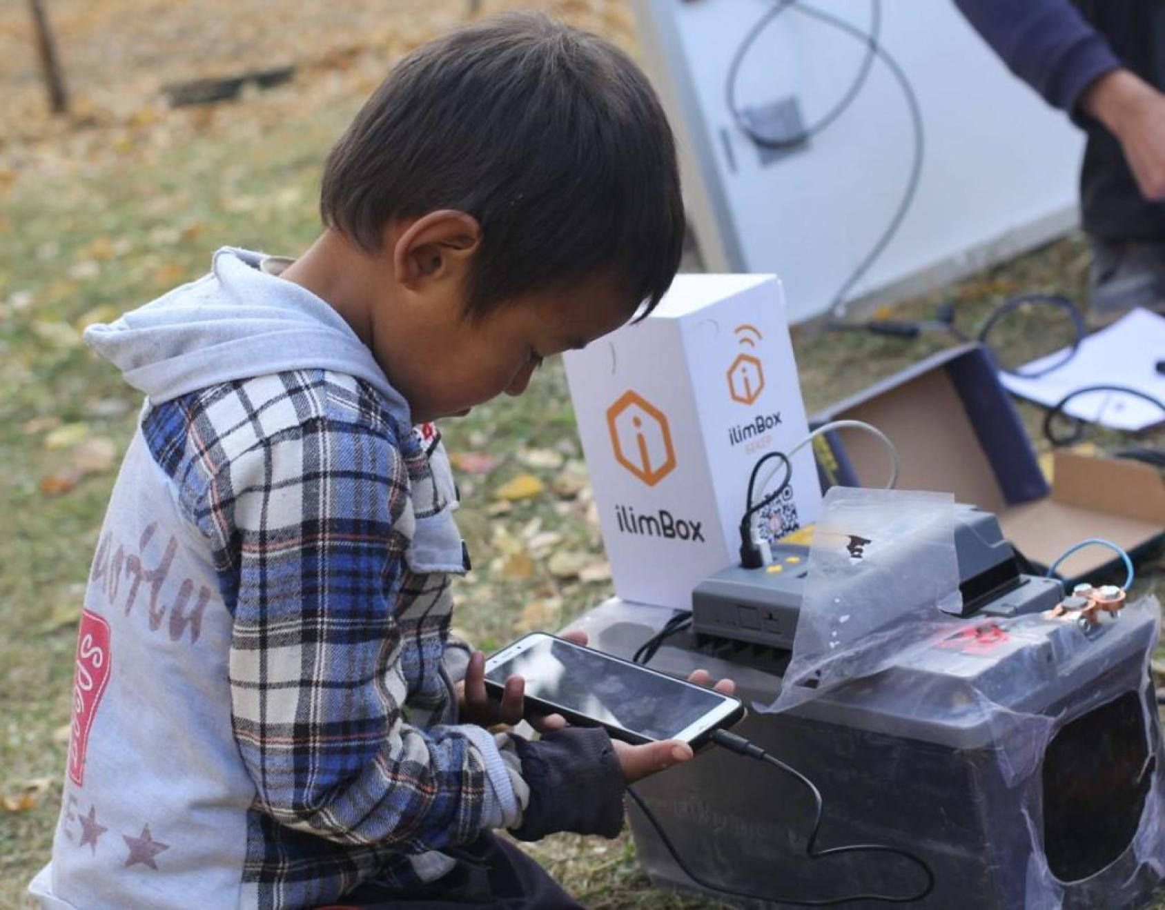 A little boy is reading from a mobile phone screen. 