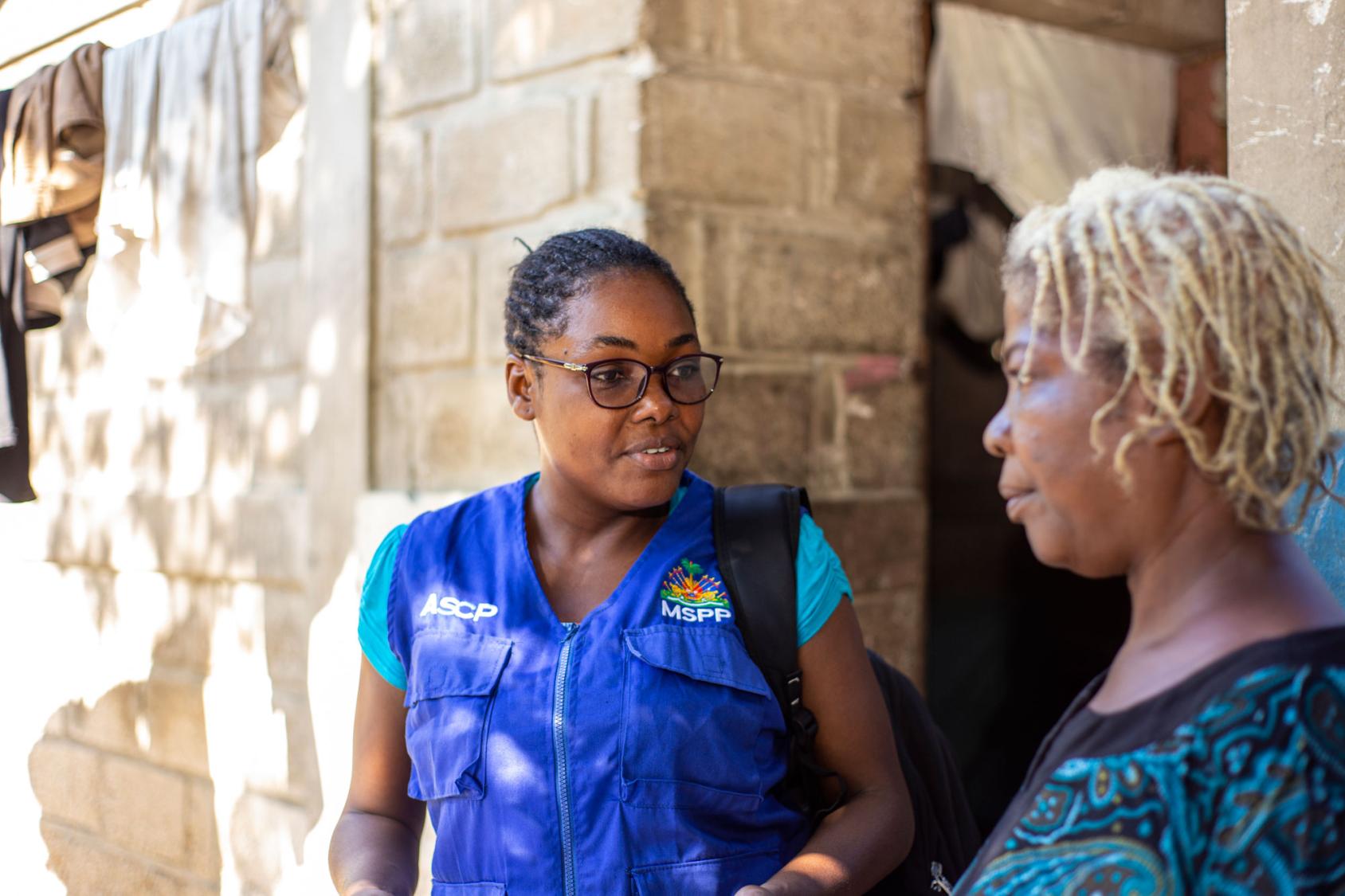 Крупный план женщины в очках, разговаривающей с другой женщиной с обесцвеченными волосами.