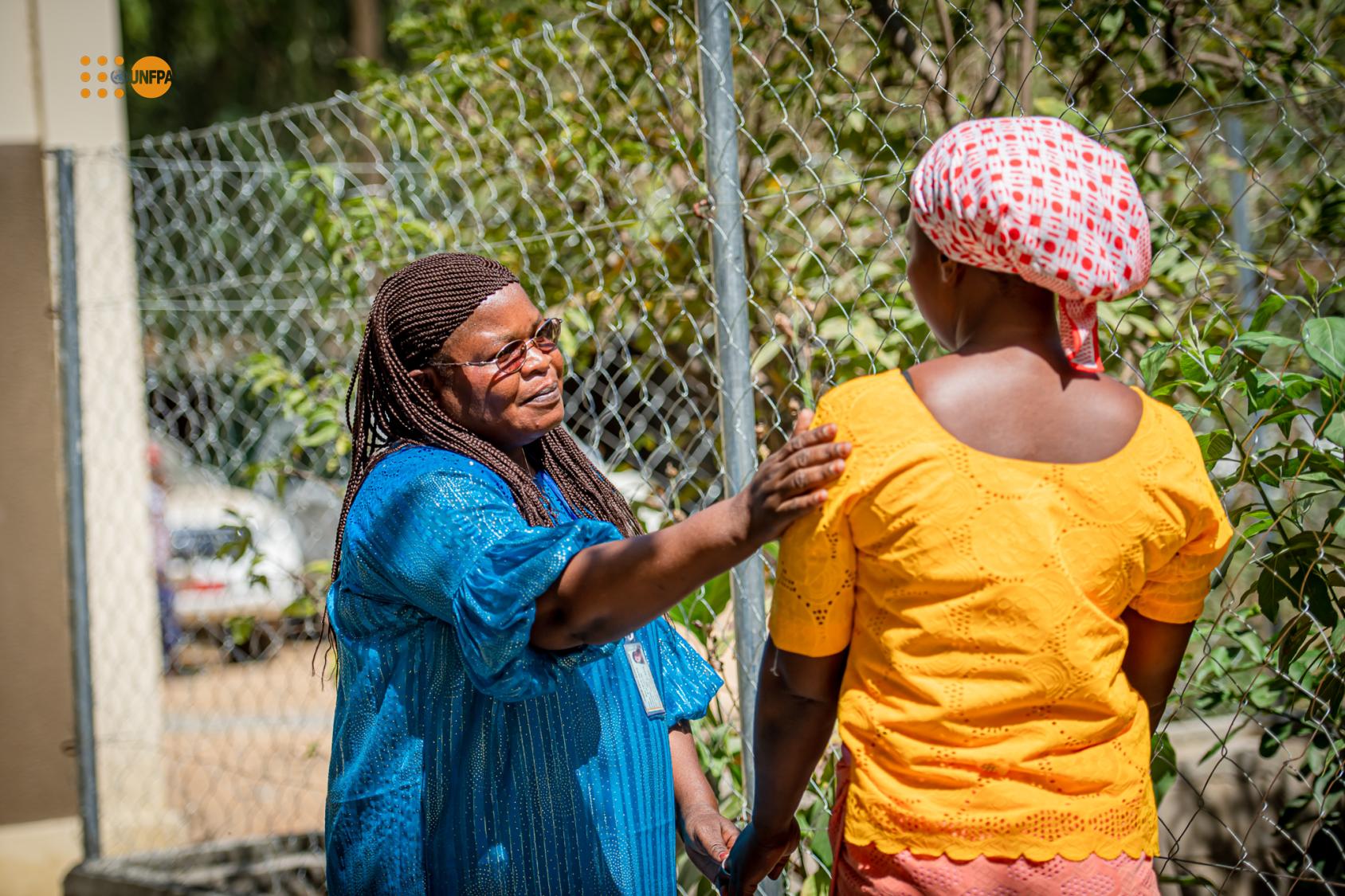 Une femme en robe bleue debout avec son bras sur une femme en robe jaune