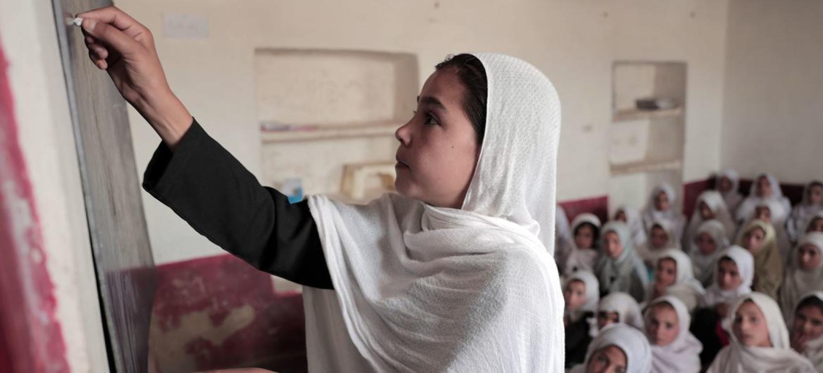 Girl in a white headscarf writing on a blackboard in a classroom
