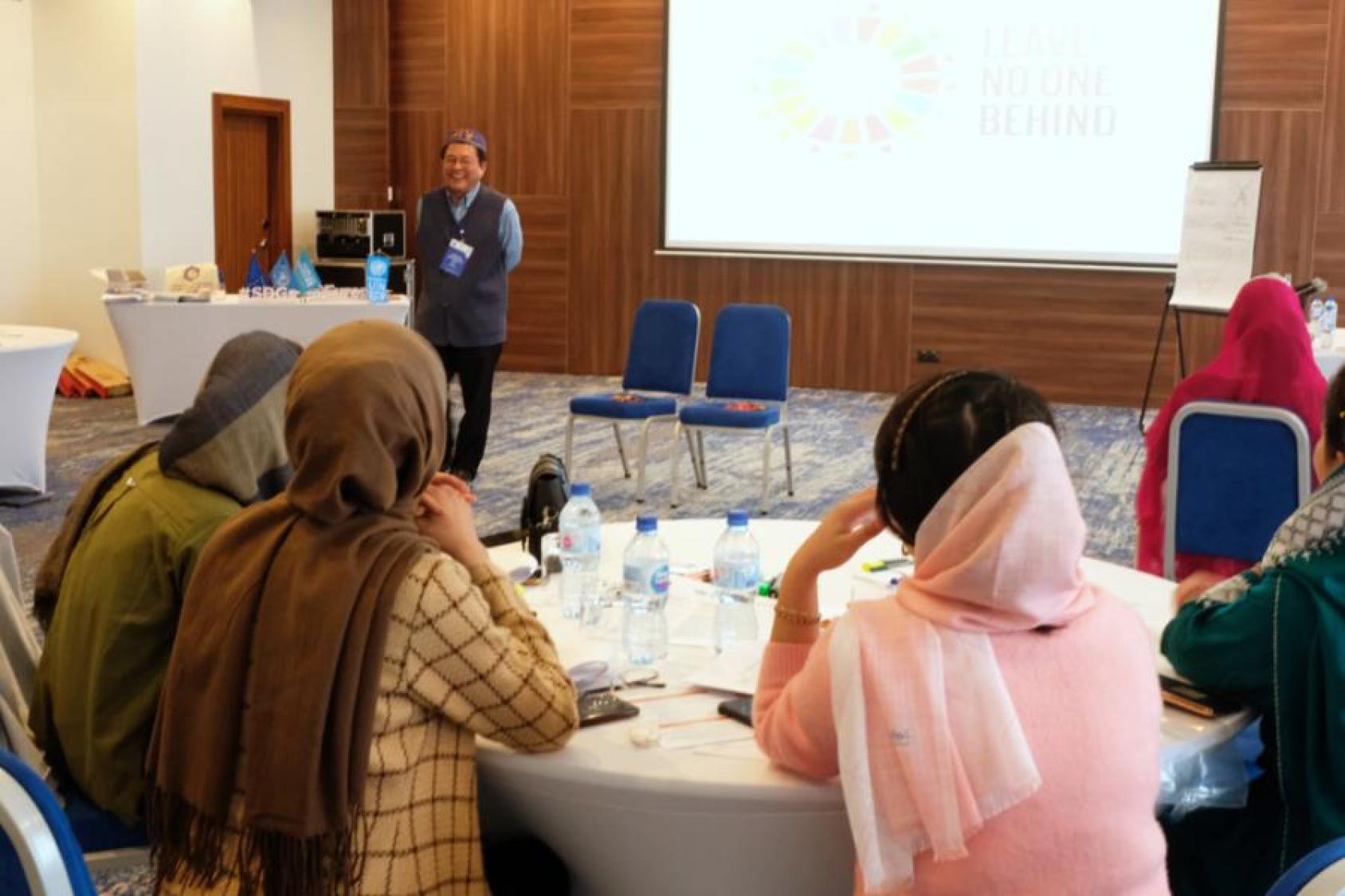Women in headscarves loosely draped over their shoulders and hair sit at a table at a training.