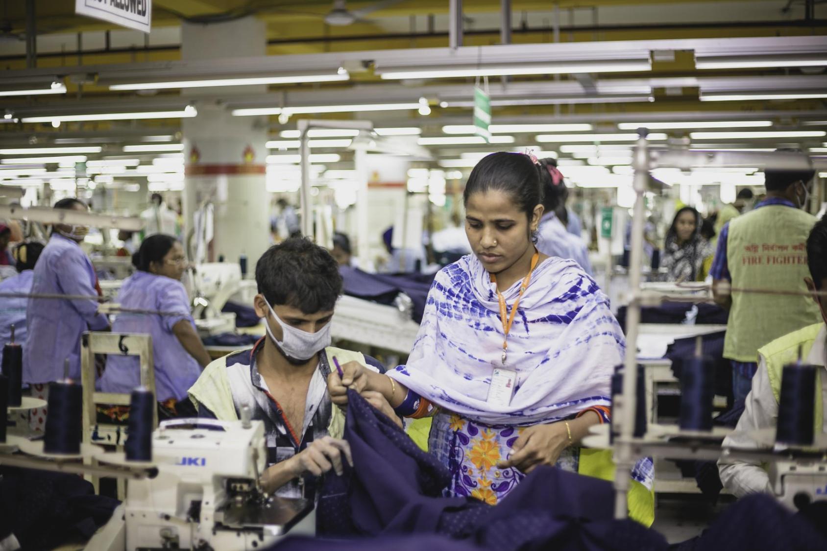 Woman in a blue shirt and a man in a facemask working at a desk and a sewing machine
