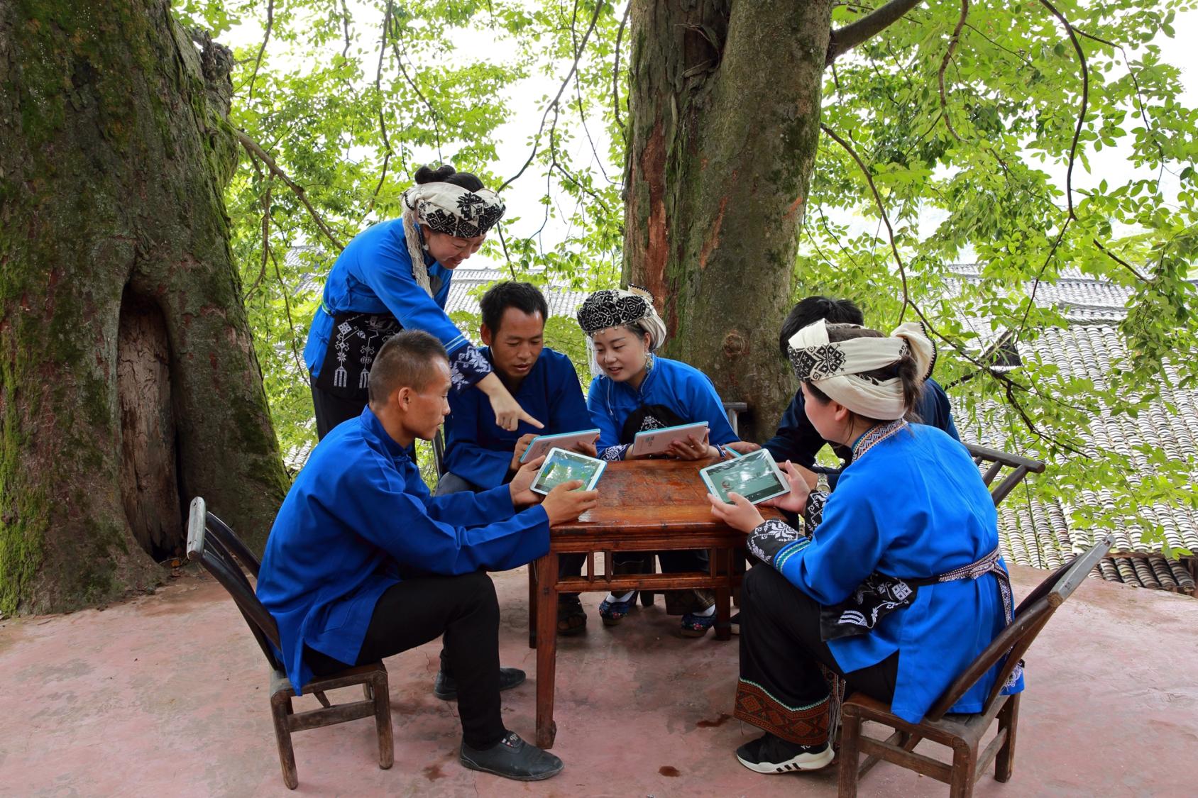 Group of people in blue clothes sitting around a table looking at computer screens animatedly