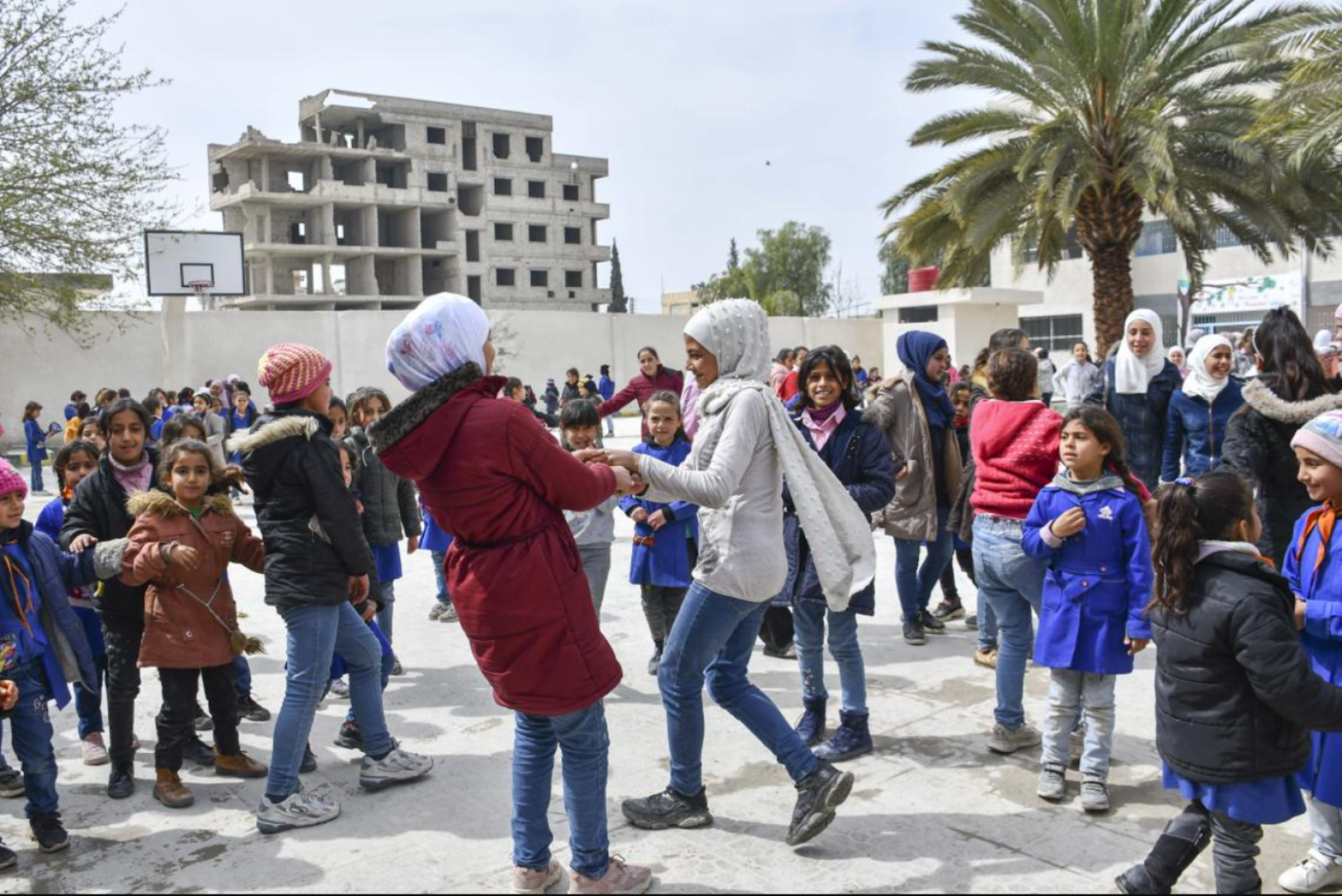 A group of children in colourful clothes and headscarves play together in a building that looks like a school